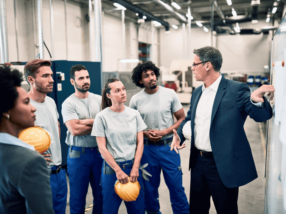 A facility manager giving presentation to group of industrial workers in a factory